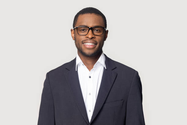Smiling african American millennial businessman in glasses isolated on grey studio background posing, satisfied successful black male in formal suit wearing spectacles look at camera laughing