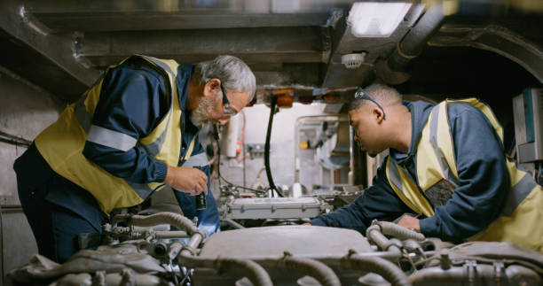 istockphoto-1415438657-612x612 Mechanics at work, fixing and concentrating on engine an in repair. Two men wearing overall uniforms on the job in a large workshop. At the auto service, male colleagues examine a motor in a garage.